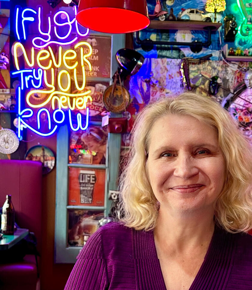 A picture of a blonde woman in a restaurant with a neon sign and other decorations in the background.